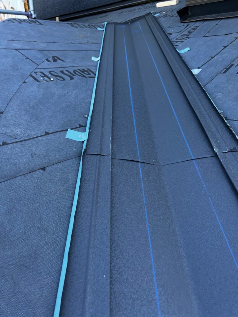 谷板金取り付け<br />
（屋根と屋根が重なり合う所を谷板金といいます。雨漏れがしやすい箇所の為、直接本体にビス打ちをせず、横に捨て板金をつけ、ビスで谷板金を固定しています。）