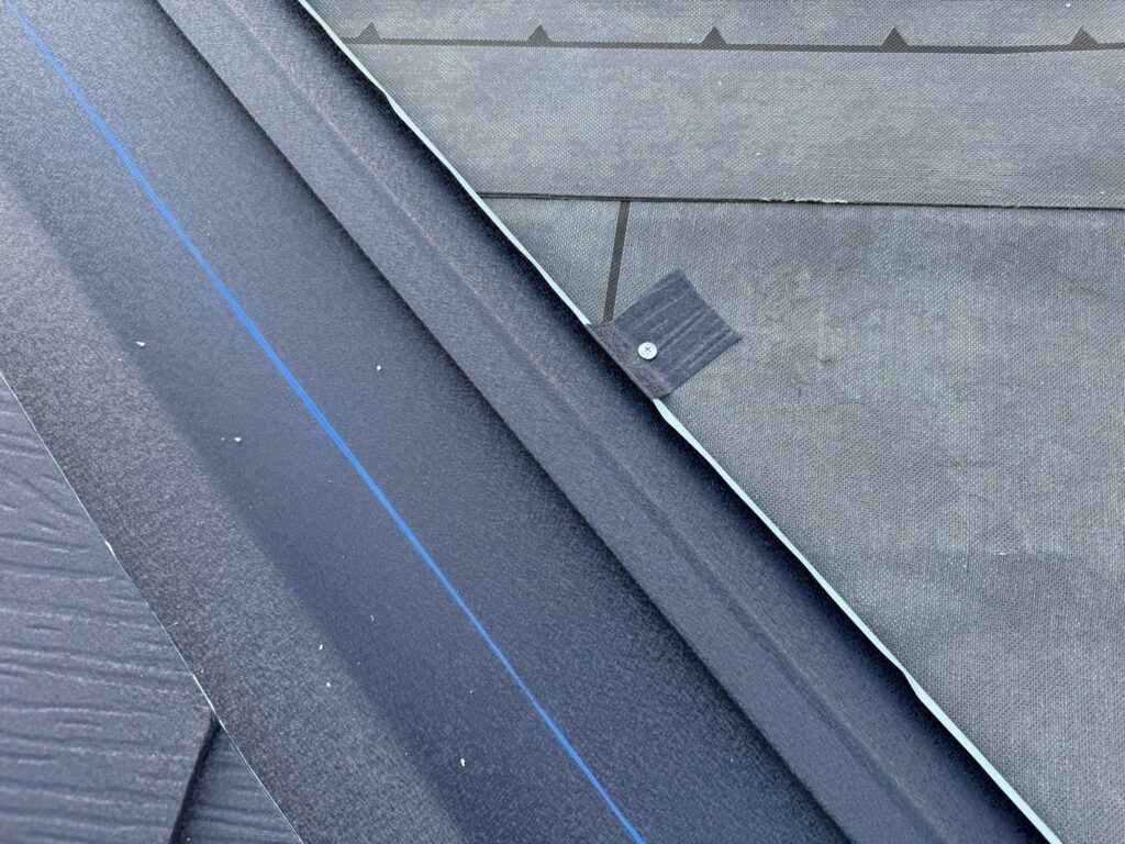 谷板金取り付け（大屋根）<br />
（屋根と屋根が重なる谷の部分に取り付ける役物です。雨の通り道となる為、直接ビス打ちはせず、横でビスにて固定をしています。これにより雨漏れのリスクが少なくなります。）
