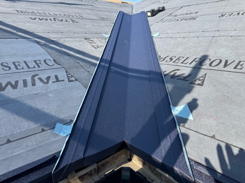 谷板金取り付け（大屋根）<br />
（屋根と屋根が重なる谷の部分に取り付ける役物です。雨の通り道となる為、直接ビス打ちはせず、横でビスにて固定をしています。これにより雨漏れのリスクが少なくなります。）